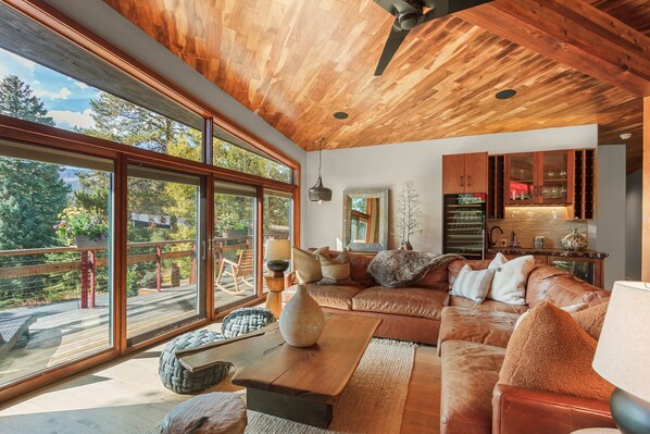 A spacious living room with a large wooden ceiling, a leather sofa, a dining area, and a kitchen with wooden cabinets.