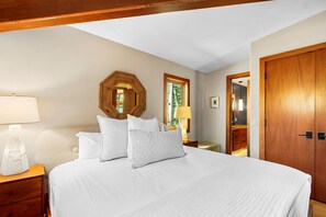 A bedroom with a large bed, wooden headboard, a wooden door, and a window with a view of trees.