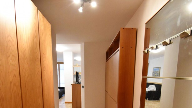 Een smalle gang met houten kasten, een betegelde vloer en een deur naar een andere kamer.