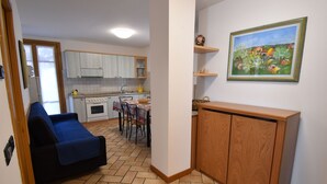 Een compacte keuken met witte kastjes, een eettafel en een blauwe bank in de woonkamer.