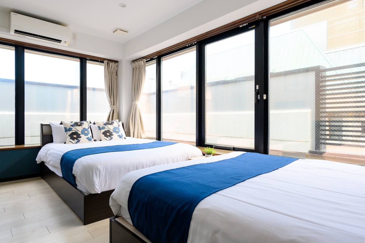 A hotel room with two beds, large windows, and a view of the outside.