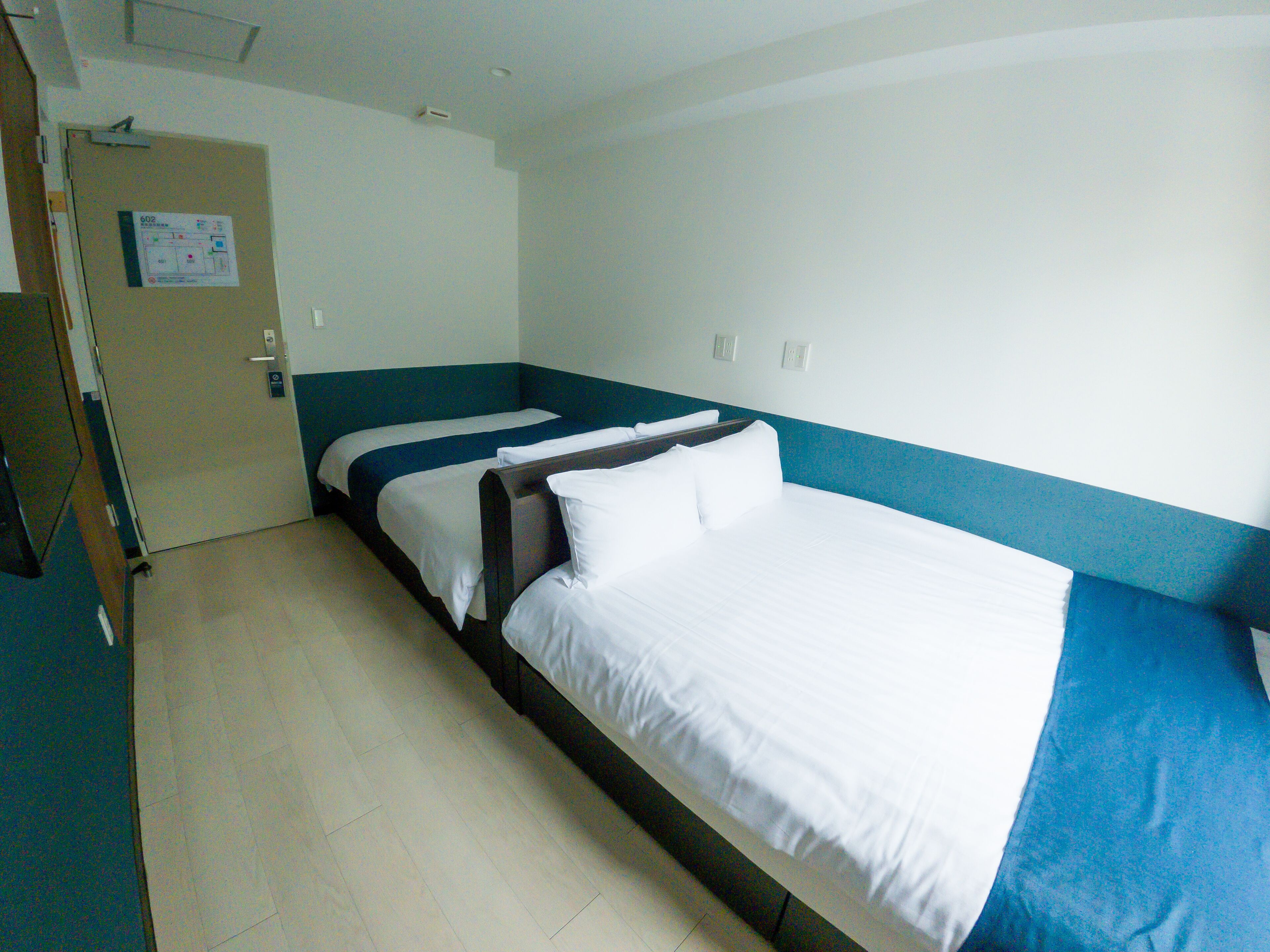 A hotel room with a single bed, a wooden door, and a light-colored tiled floor.