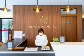 A hotel reception desk with a wooden backdrop, a receptionist, and a QR code for digital check-in. - UENO WOO HOTEL (Tokyo)