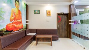 Un vestíbulo moderno con un sofá de cuero marrón, una mesa de centro de madera y un mural de Buda. Hay dos obras de arte enmarcadas en la pared y un letrero para el salón de banquetes.
