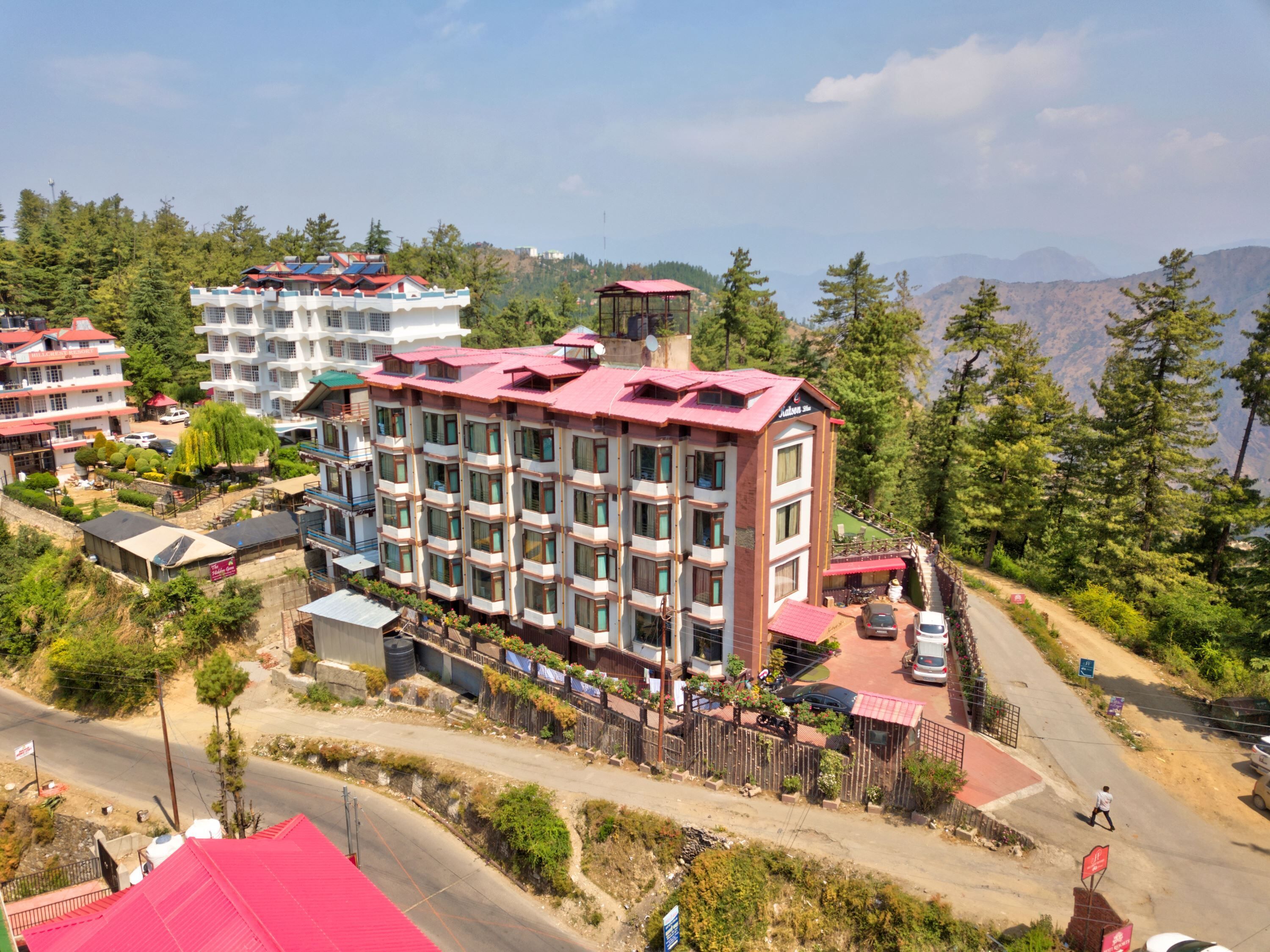 Un hotel de varios pisos con techo rojo, rodeado de vegetación y montañas al fondo.