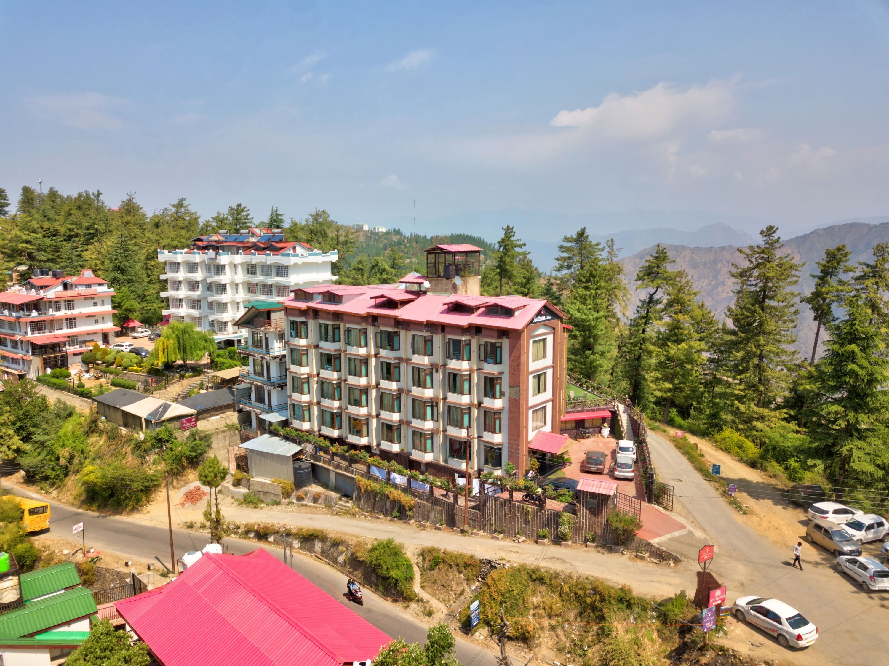 A multi-story hotel with a red roof, surrounded by lush greenery and mountains in the background.