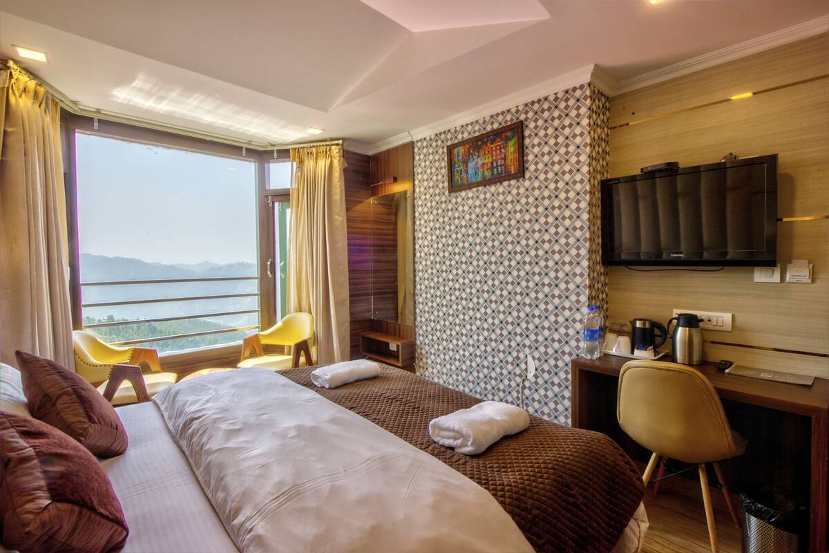 A hotel room with a large bed, a desk with a TV, a chair, and a view of the mountains.