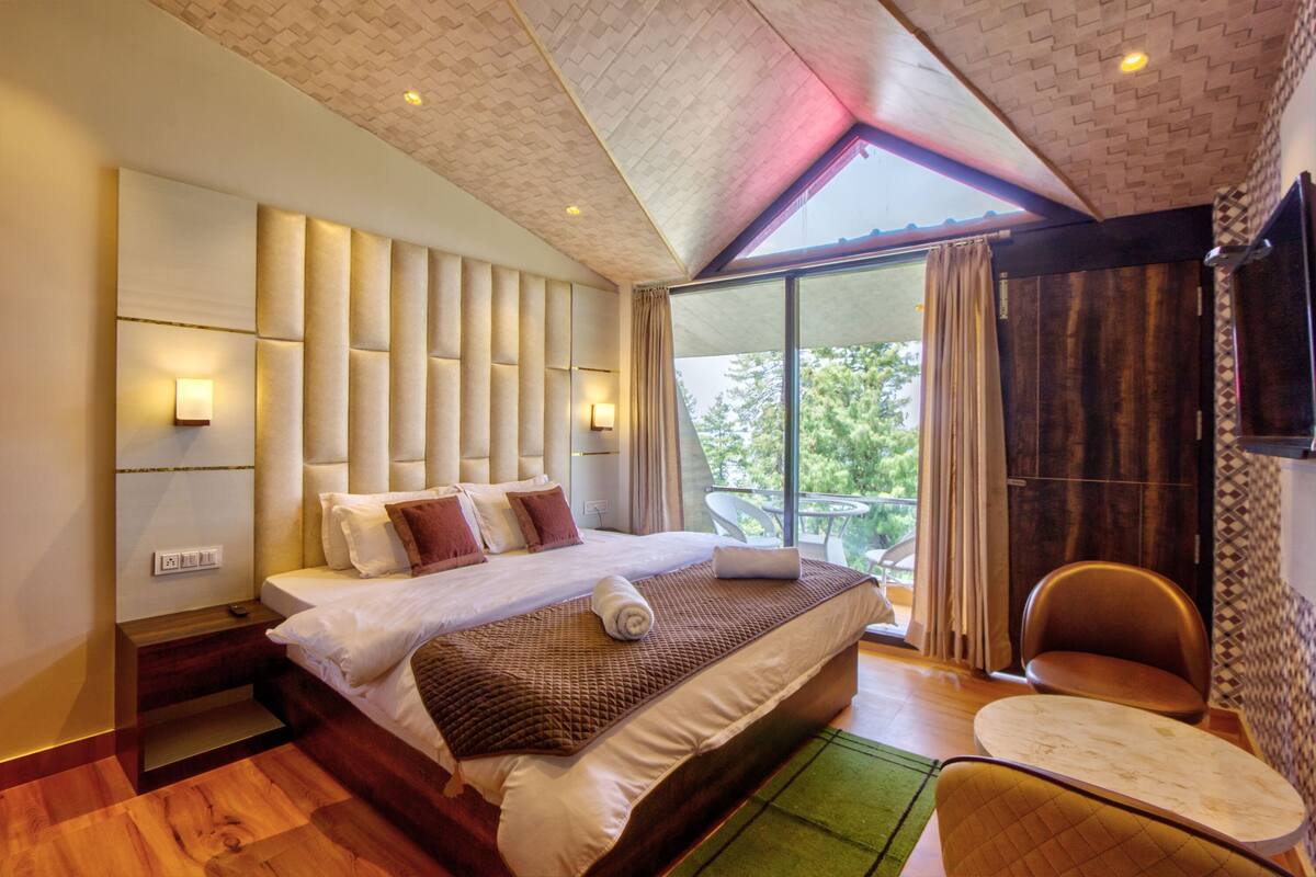 A modern bedroom with a large bed, a seating area, and a balcony with a view.