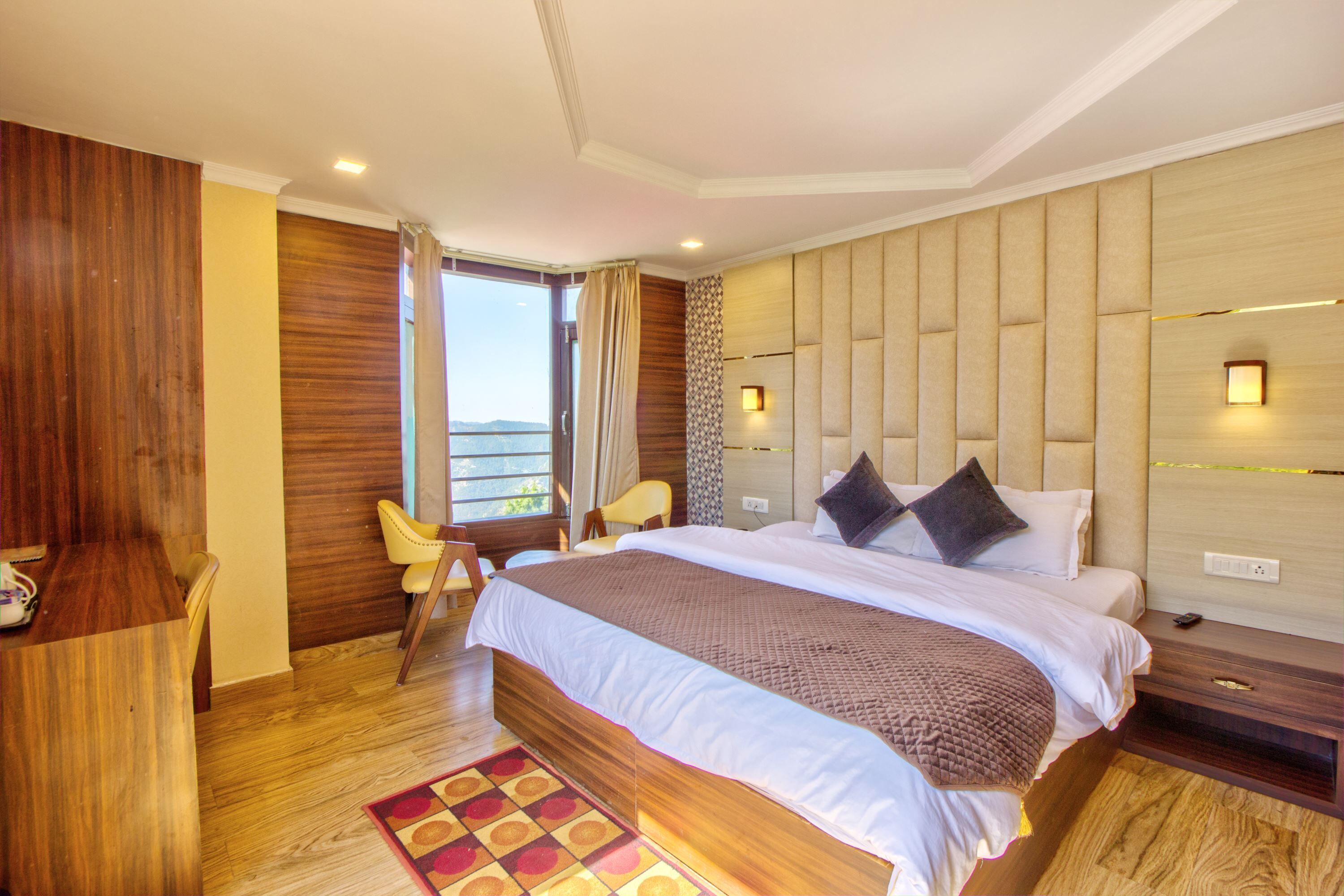 Una habitación de hotel moderna con una cama grande, paneles de madera, vistas al balcón y un pequeño rincón de estar.