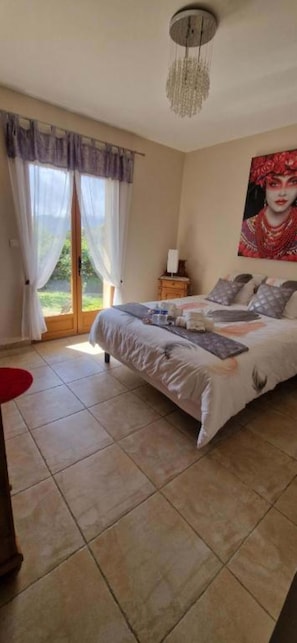 Un dormitorio con una cama, una mesita de noche, un cuadro y una ventana con cortinas.