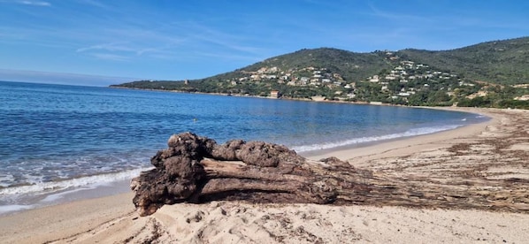 Una playa con una gran formación rocosa en primer plano y un paisaje montañoso al fondo.