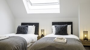 A bedroom with two beds, a skylight, and bedside lamps.