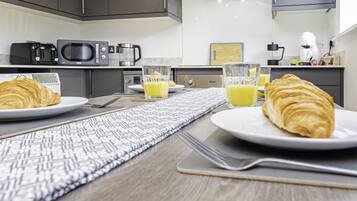A breakfast setup with croissants, orange juice, and a coffee maker in a modern kitchen.