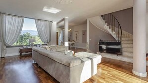 A spacious living room with a large sofa, wooden flooring, a staircase, and a view of the outdoors. - Villa with private pool in The Tuscan Countryside (Figline e Incisa Valdarno)
