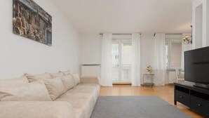 Un salon avec un canapé beige, un tapis gris, un meuble TV noir et un tableau accroché au mur.