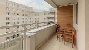 Un balcon avec une table et des chaises en bois, une vue sur les bâtiments voisins et une rambarde en métal.