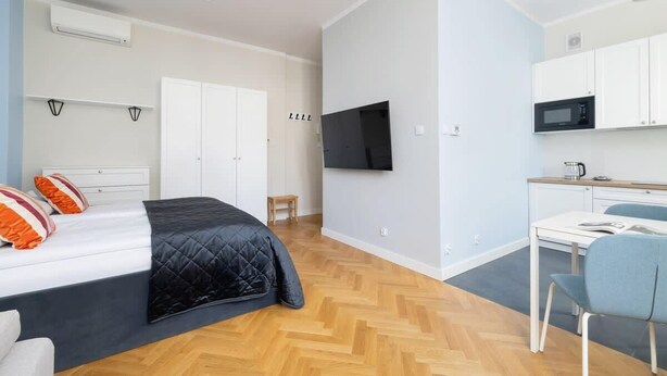 A modern hotel room with a bed, a desk, a chair, a TV, and a kitchenette. - Modern Studio in Kazimierz | 1 km from the Wawel Castle (Kraków)
