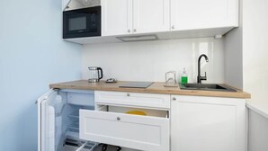 A compact kitchen with white cabinets, a microwave, a sink, and a coffee maker. - Modern Studio in Kazimierz | 1 km from the Wawel Castle (Kraków)