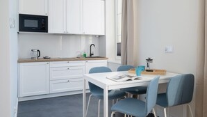 A modern kitchen with white cabinets, a microwave, and a sink. There is a dining table with blue chairs and a book on it. - Modern Studio in Kazimierz | 1 km from the Wawel Castle (Kraków)