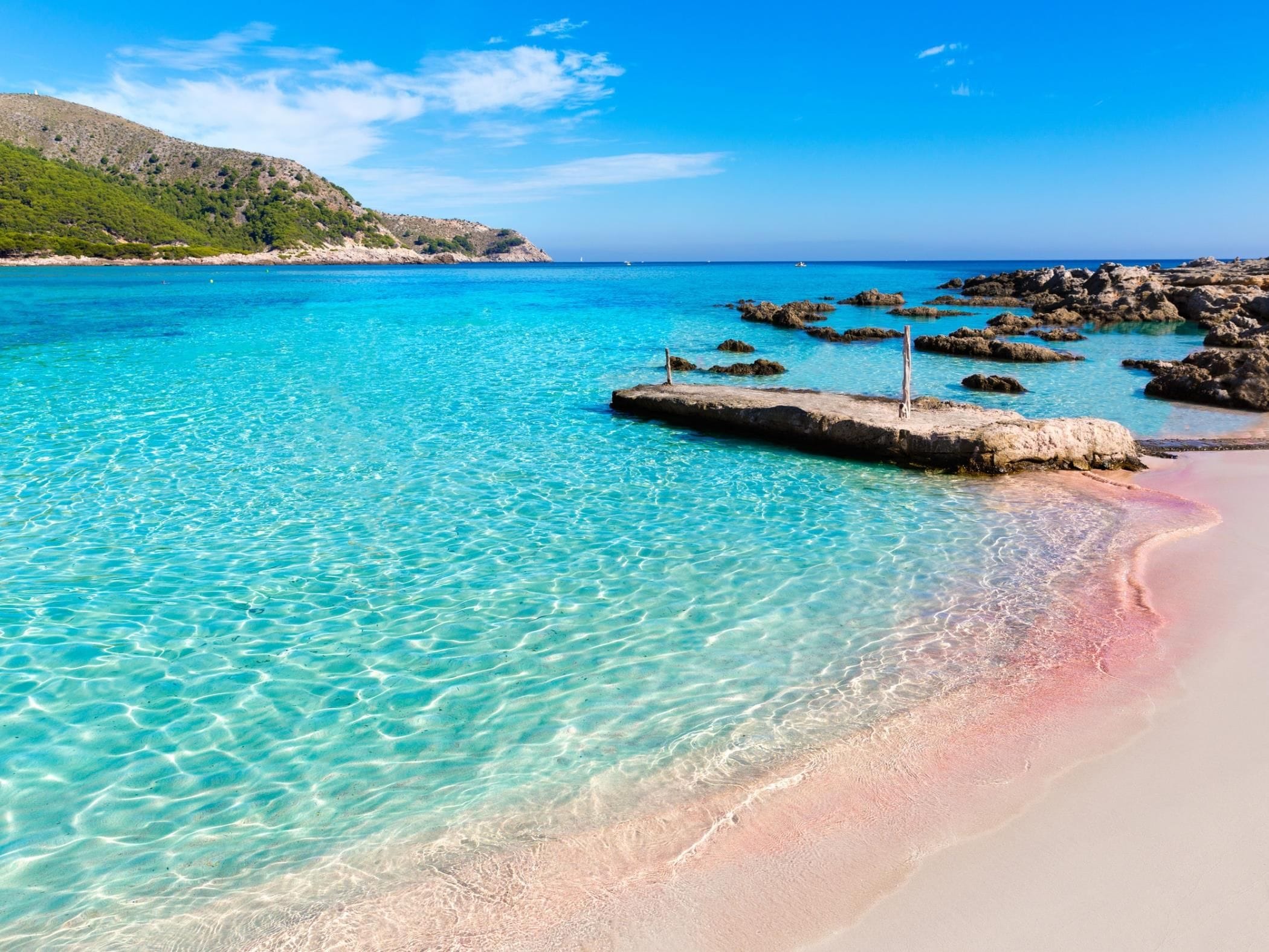 Un mar turquesa cristalino con una playa de arena y afloramientos rocosos.