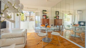 A modern dining area with a glass table, wire chairs, and a white sofa. - Apartamento Bonaire (Alcúdia)