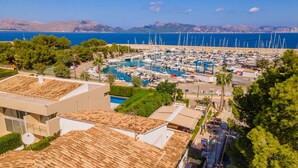 A coastal marina with boats, a swimming pool, and buildings with terracotta roofs. - Apartamento Bonaire (Alcúdia)
