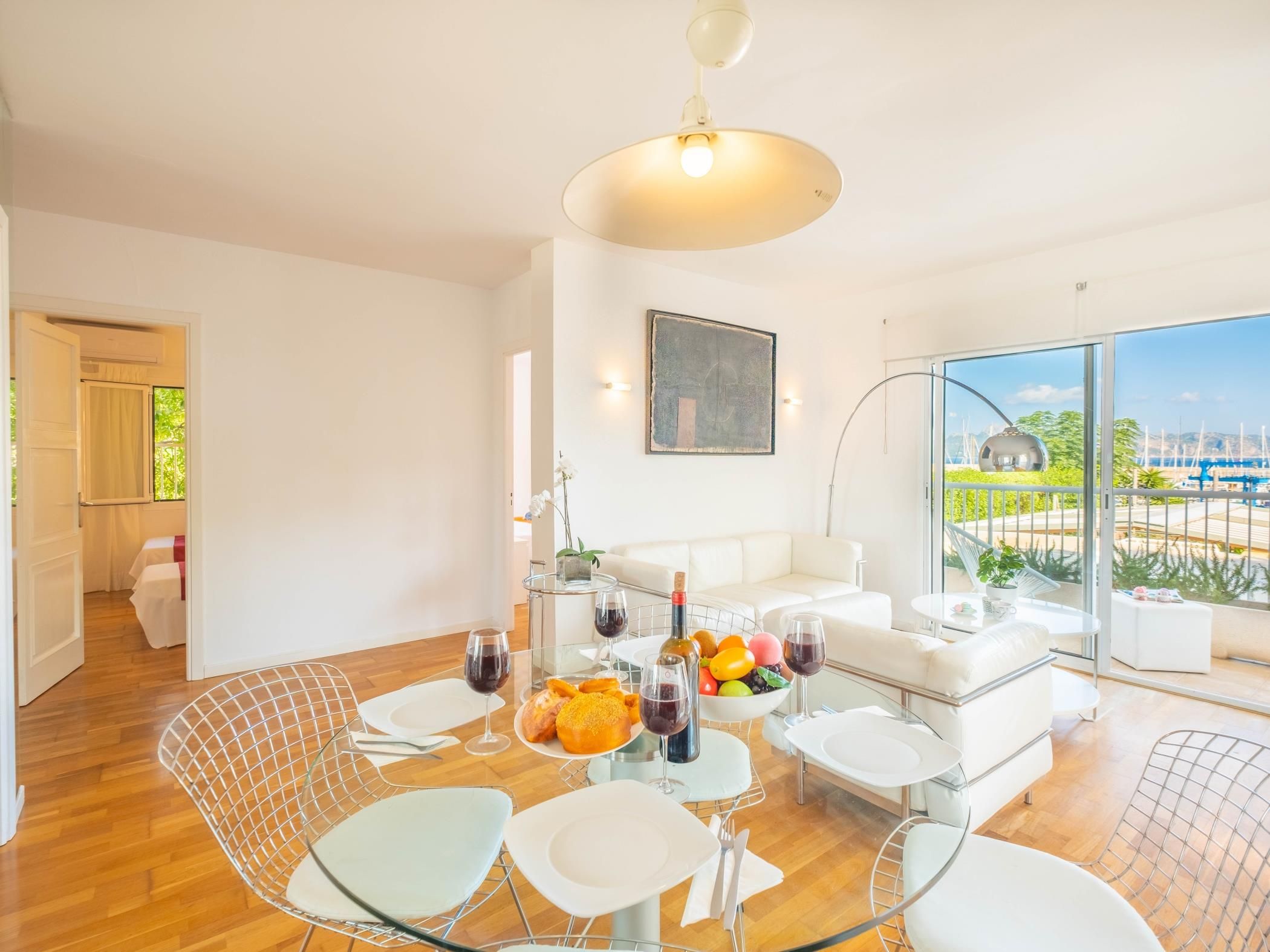 A modern dining area with a glass table, white chairs, and a view of the marina through large windows.