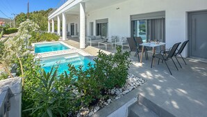 A modern outdoor pool area with a white building, outdoor seating, and a clear view of the pool. - Beach front home in Vasilika Evia (Vasilika Evia)