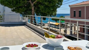 A balcony with a table set for breakfast, overlooking a coastal area with a view of the sea and buildings. - Beach front home in Vasilika Evia (Vasilika Evia)