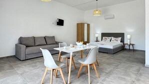 A modern, well-lit room with a grey sofa, a dining table with chairs, a bed with a grey headboard, and two pendant lights. - Beach front home in Vasilika Evia (Vasilika Evia)