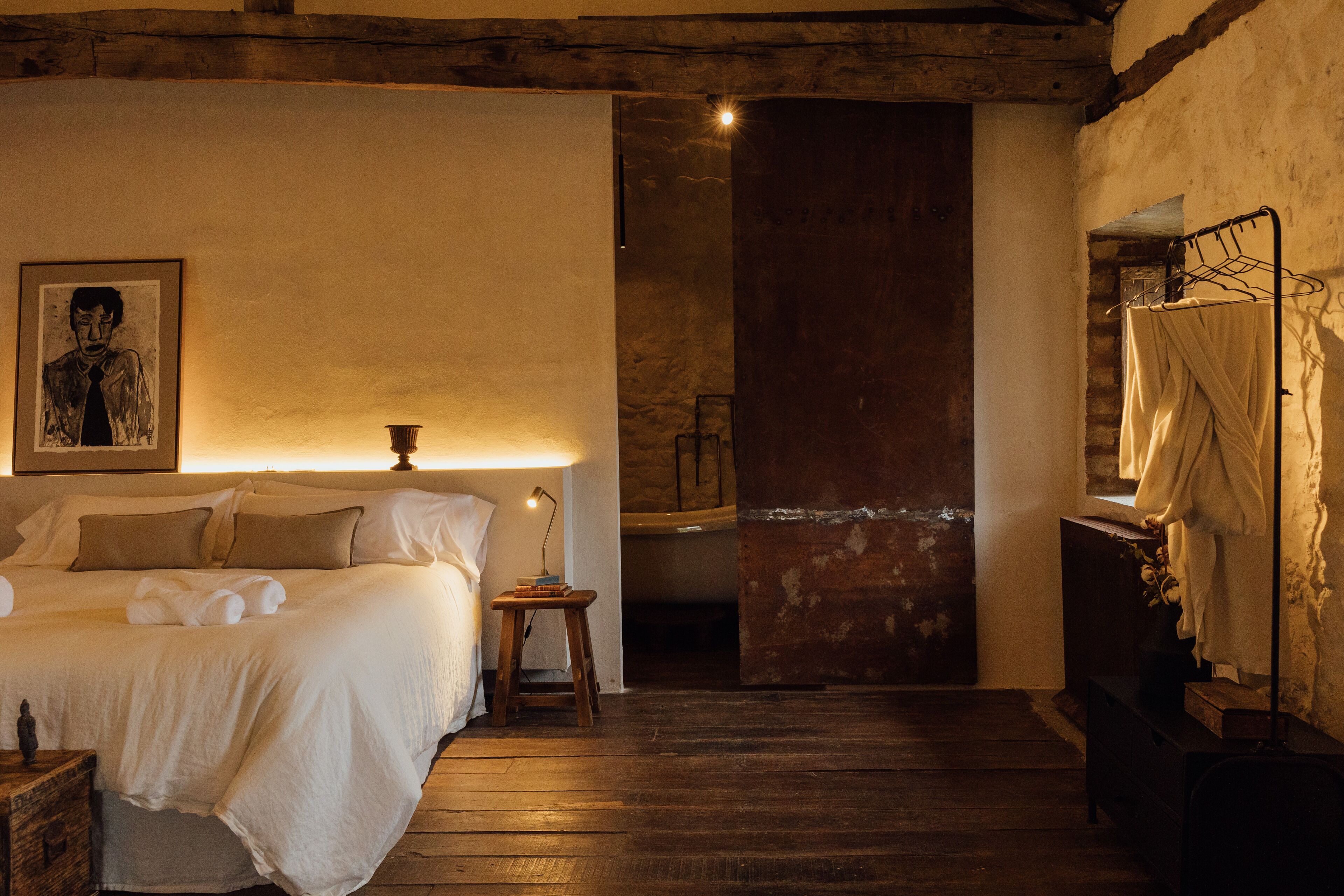A cozy bedroom with a bed, bedside table, lamp, and a framed picture on the wall.