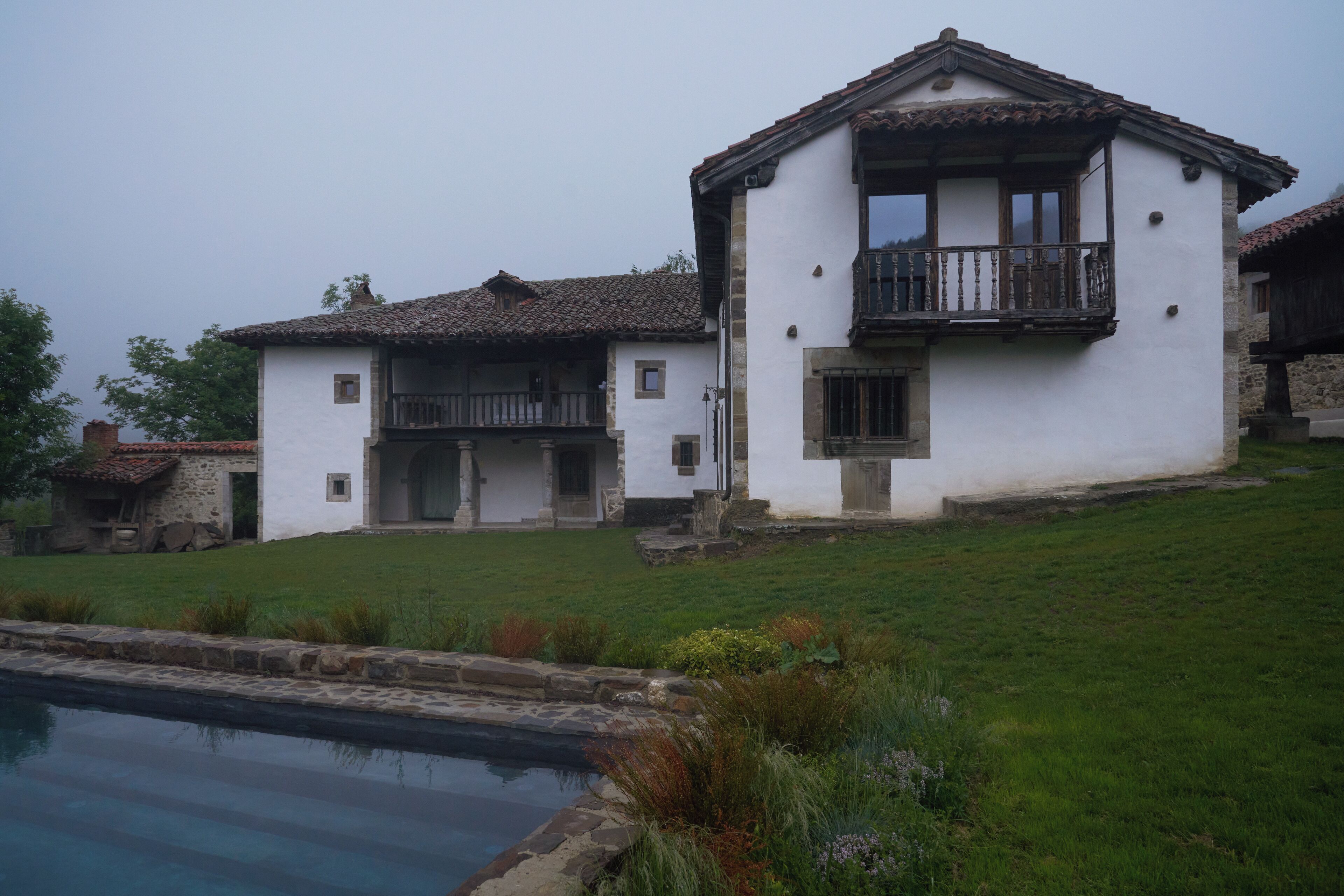 A two-story white building with a balcony, a stone pathway, and a small pool.