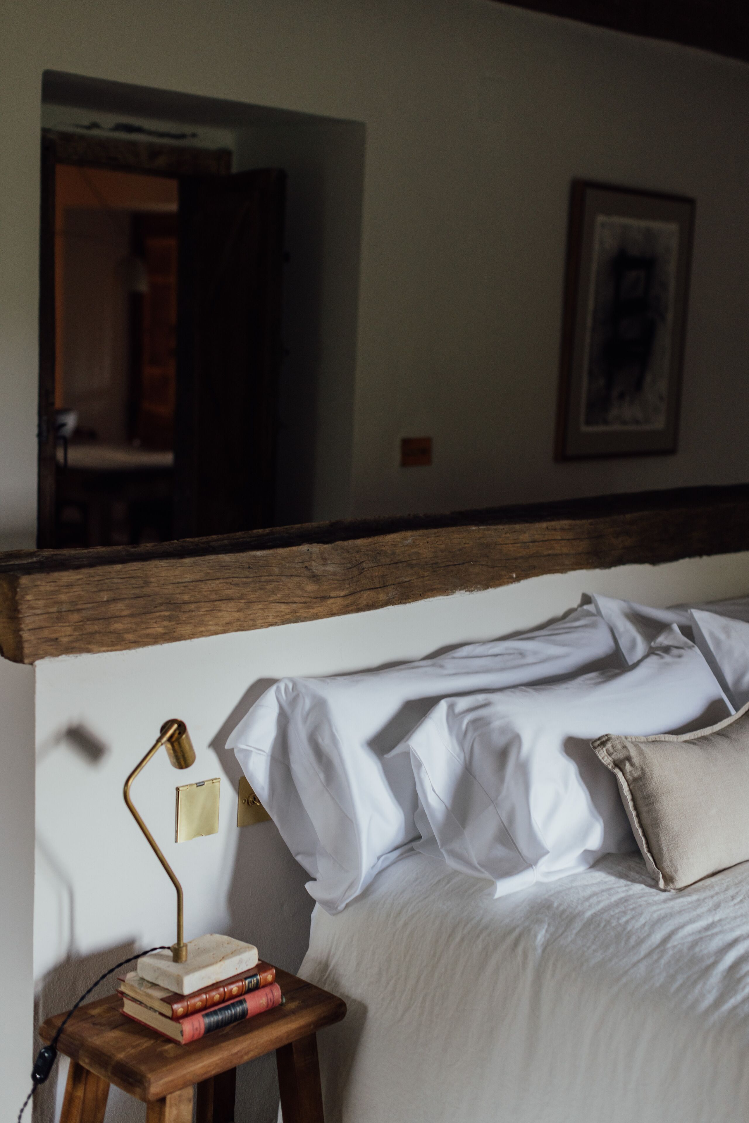 A bedroom with a wooden headboard, a bedside table with books, a lamp, and a bed with white linens.
