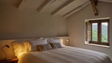 Un dormitorio con una cama grande, una mesita de noche con lámpara y una ventana con vistas a zonas verdes.