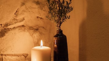 Escena iluminada por velas con un florero de plantas secas y dos velas encendidas sobre una pared con textura.