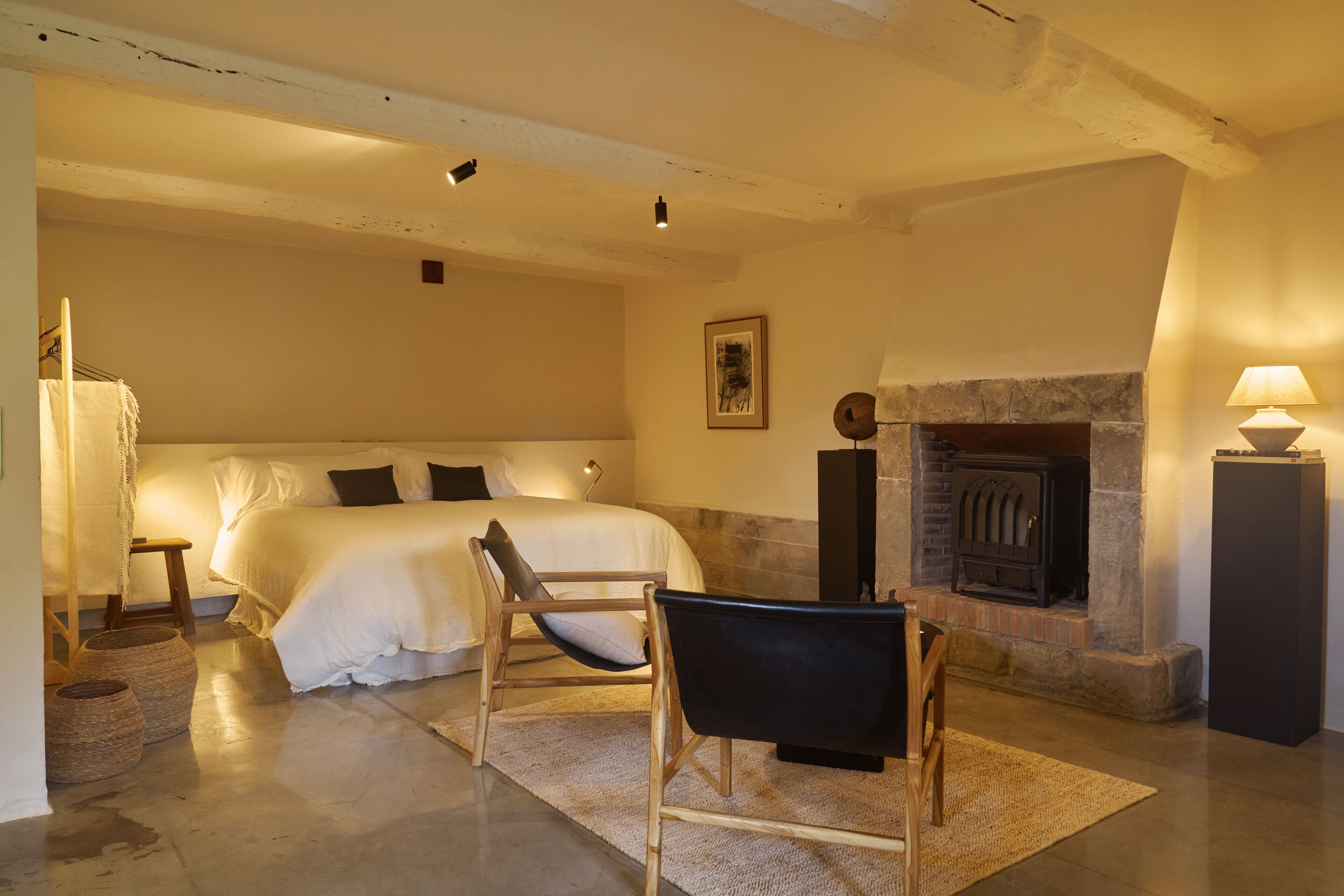 Un dormitorio con una cama, una silla, una chimenea y una lámpara.