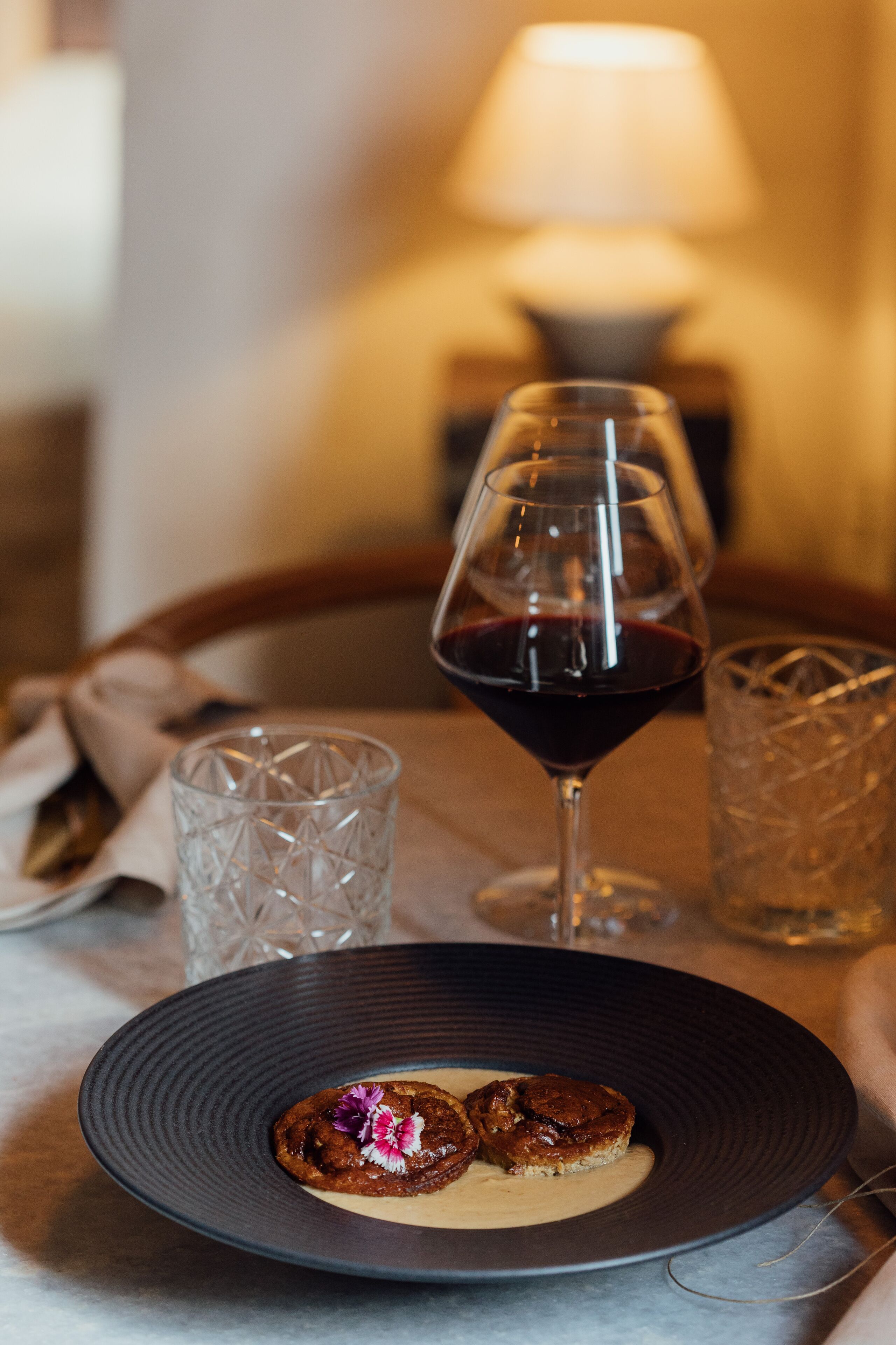 Una mesa con un plato de comida, una copa de vino tinto y dos copas de cristal.