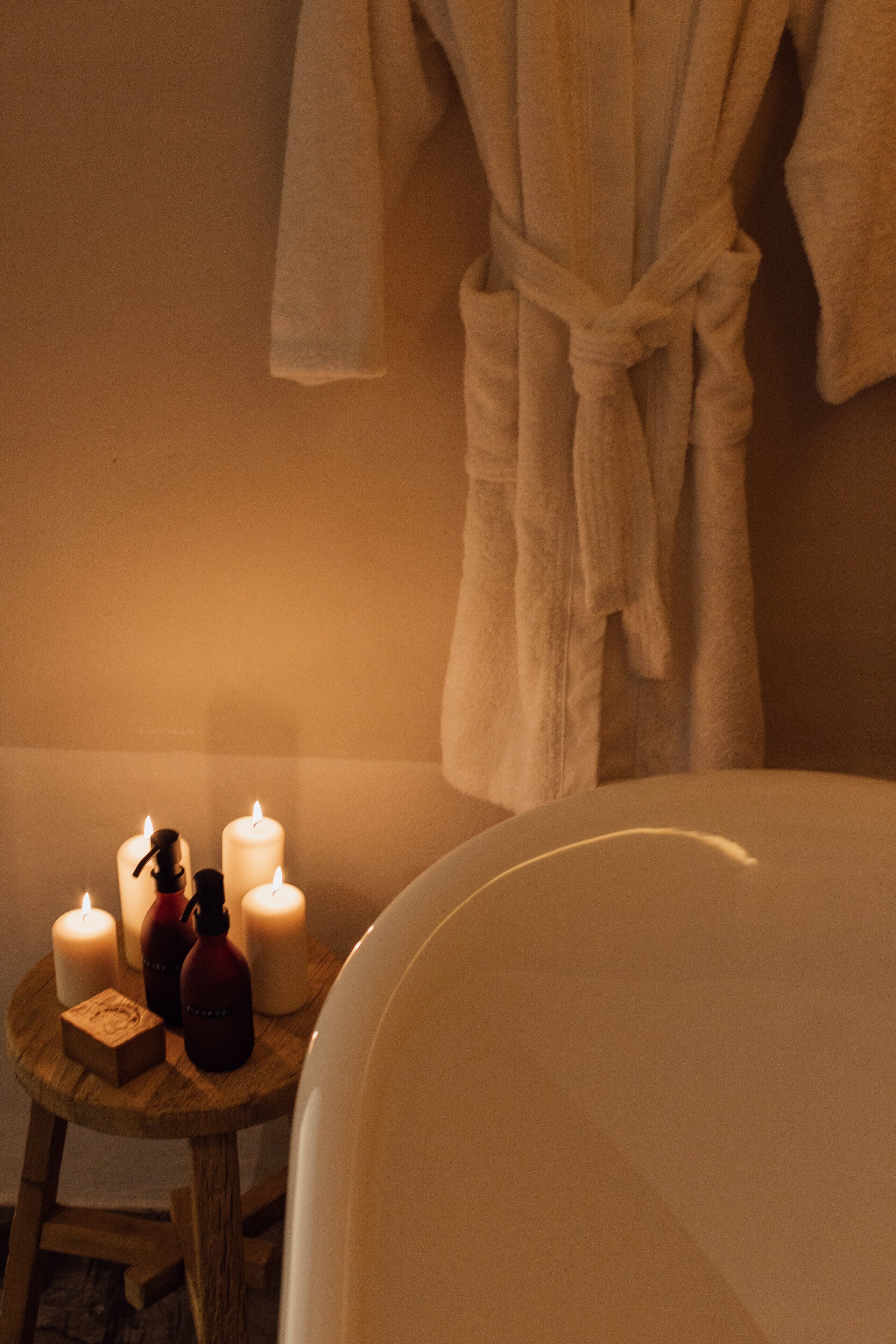 Un baño con una bañera, un taburete de madera con velas y una bata colgada en la pared.