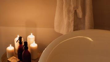 Un baño con una bañera, un taburete de madera con velas y una bata colgada en la pared.
