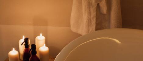 Un baño con una bañera, un taburete de madera con velas y una bata colgada en la pared.