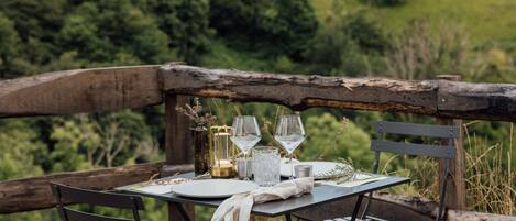 A wooden deck with a table set for two, overlooking a lush green hillside.
