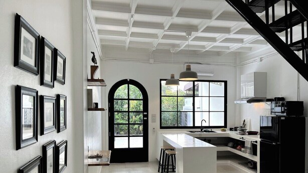 A modern kitchen with a central island, black-framed pictures on the wall, and a staircase leading to another level. - Your Local Spacious 3-story Home, Rooftop views & King Beds near Night Bazaar (Chang Wat Chiang Mai)