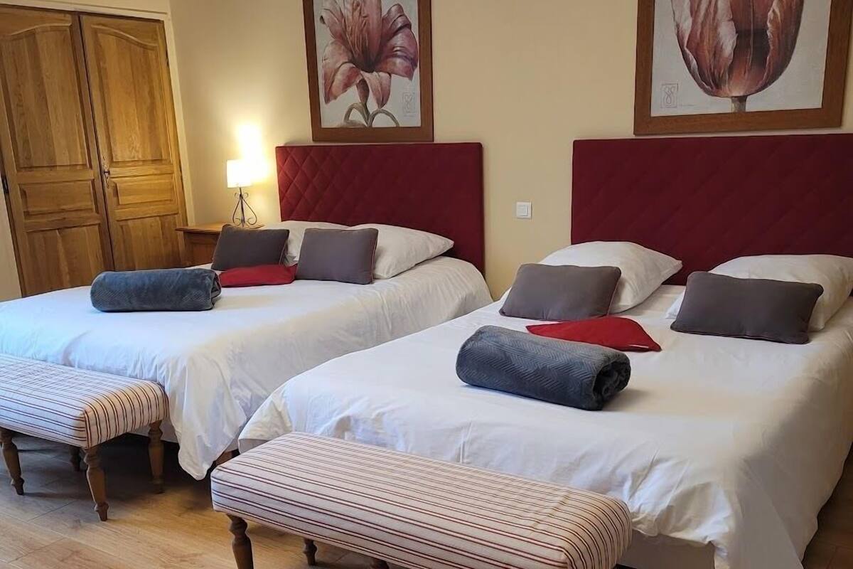 A hotel room with two beds, wooden flooring, and a bench.