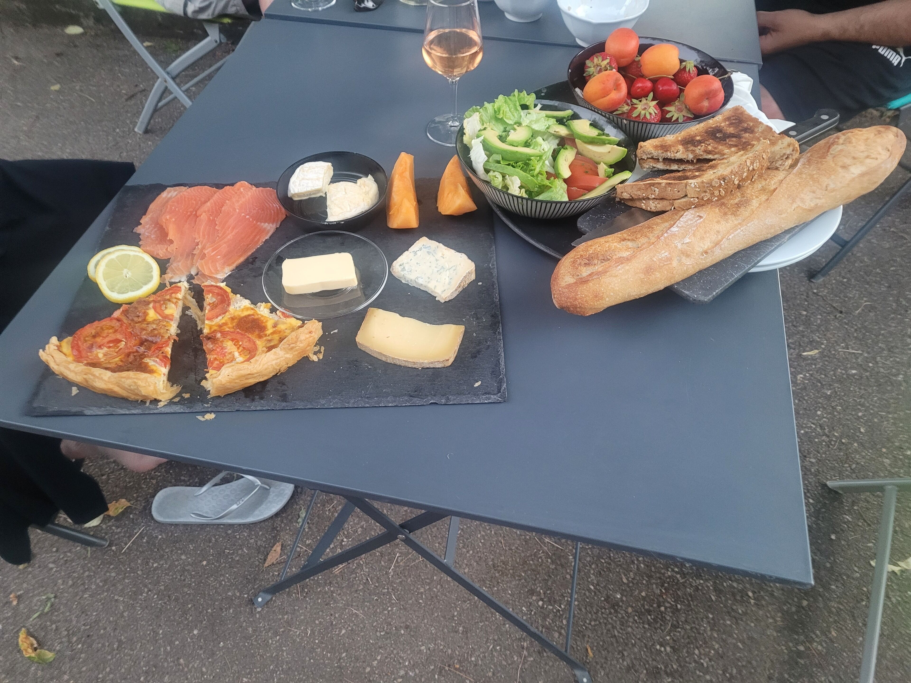 Un repas composé de différents fromages, d’une part de pizza, de saumon fumé, de pain et d’une salade, le tout disposé sur une table portable.