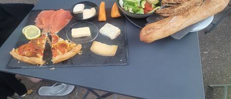 A meal setup with various cheeses, a slice of pizza, smoked salmon, bread, and a salad on a portable table.