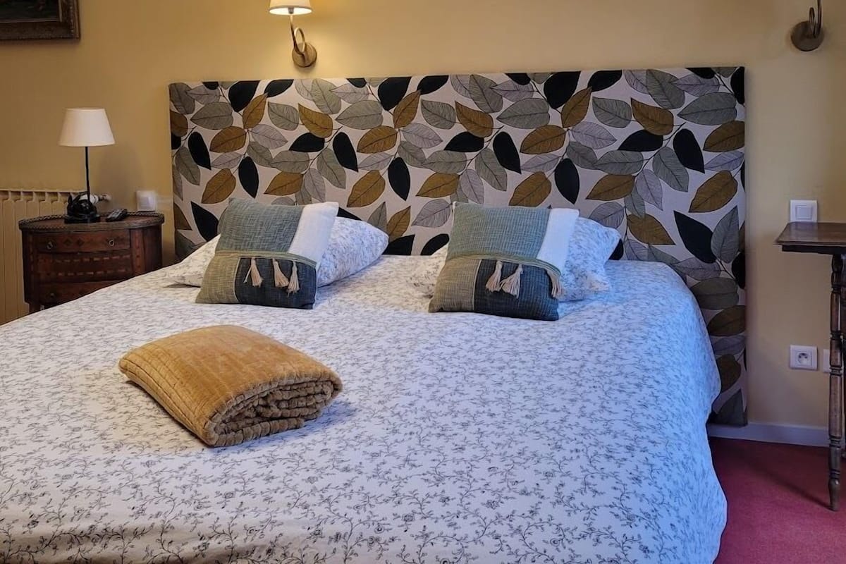 A bedroom with a bed, pillows, a bedside table, and a wall-mounted lamp.