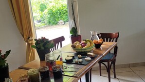 A dining table set with various food items, a potted plant, and a window with curtains. - Le cèdre bleu (Saint-Lattier)