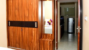 Un armario de madera con espejo, una cama con almohadas y un refrigerador al fondo.