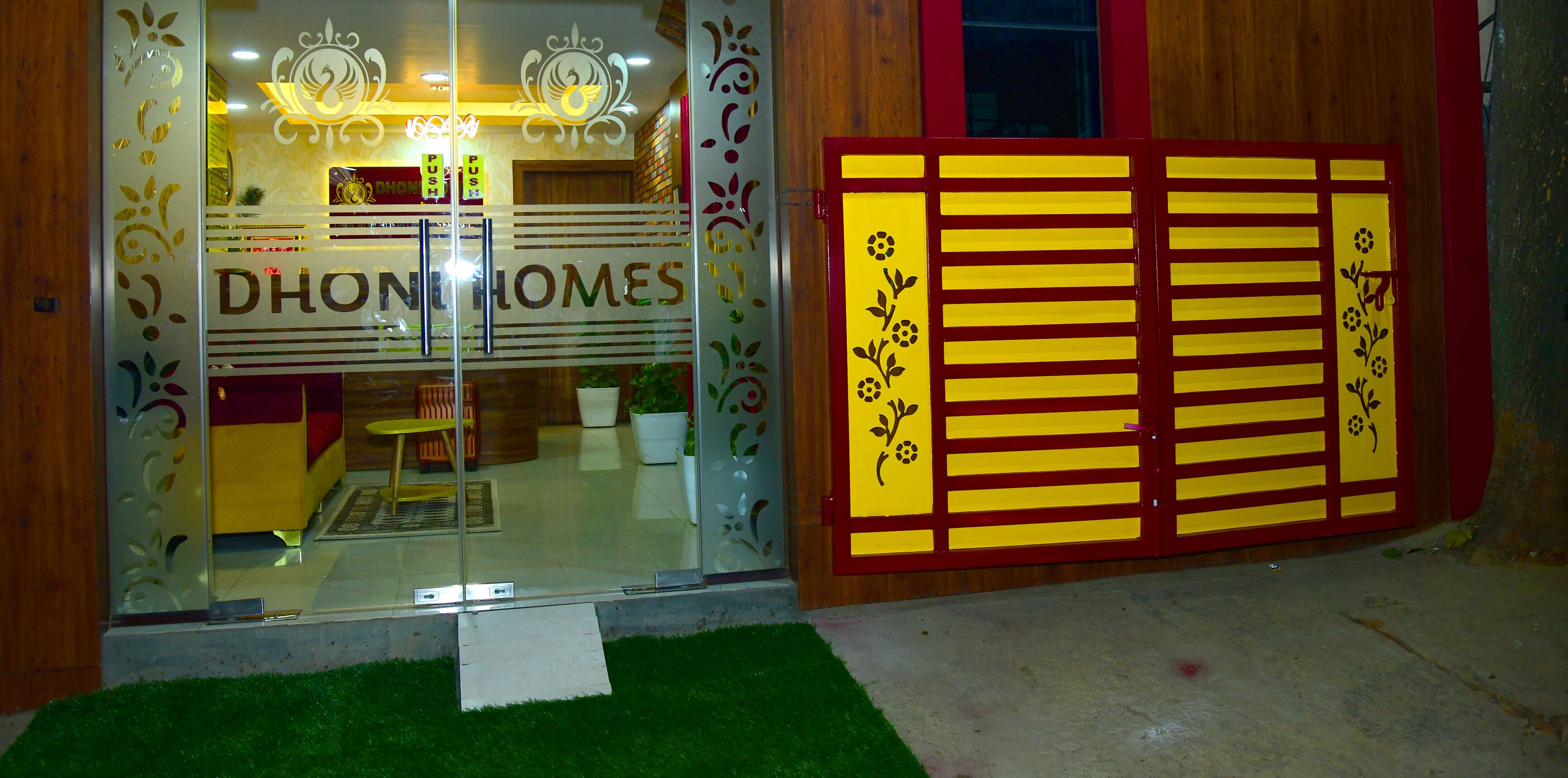 A storefront with a glass entrance, a sign reading "DHON HOMES", and a decorative yellow gate with floral patterns.