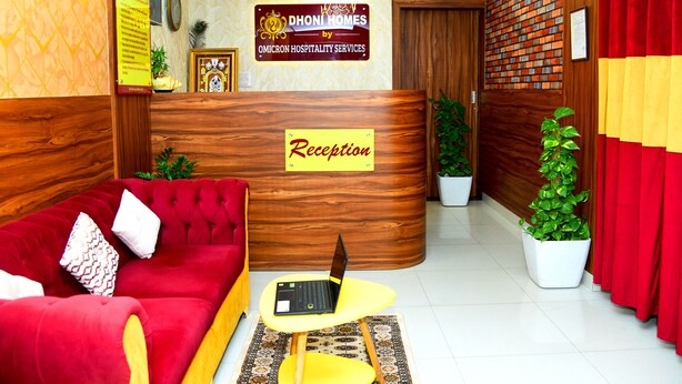 Un área de recepción con un sofá rojo, un mostrador de madera y una computadora portátil sobre una mesita.